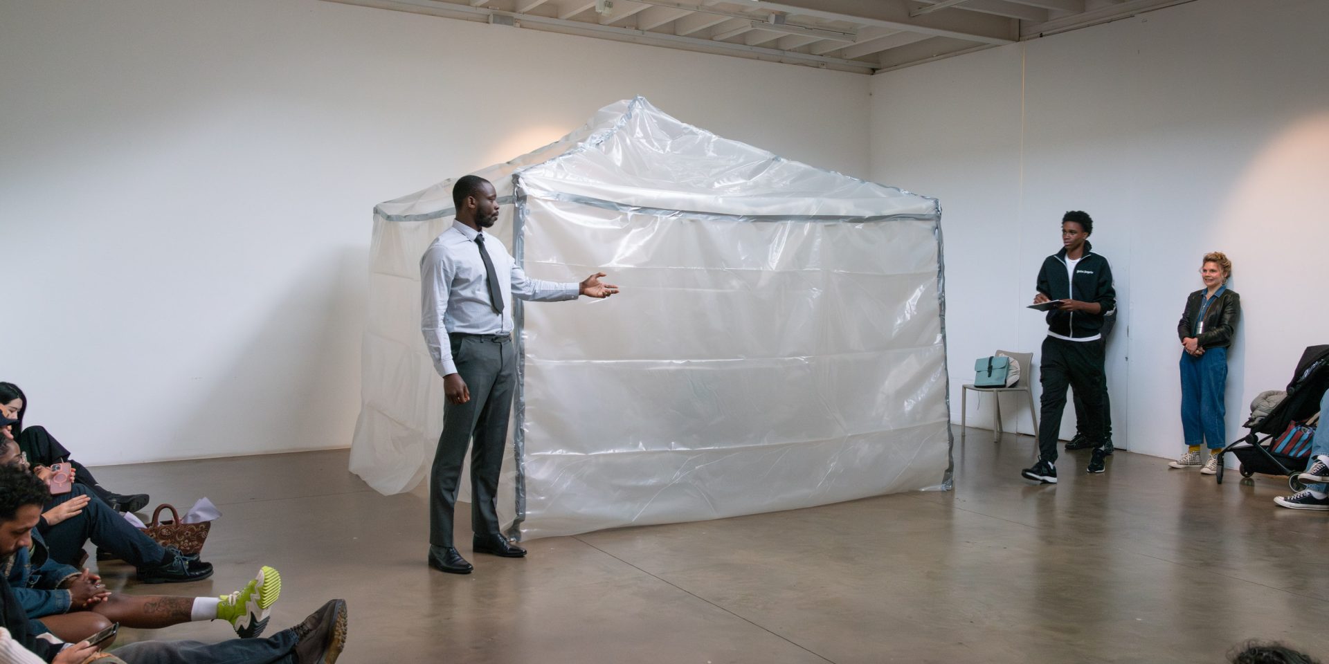 Artist Motunrayo Akinola performs in a bright white room with people sitting on the ground.