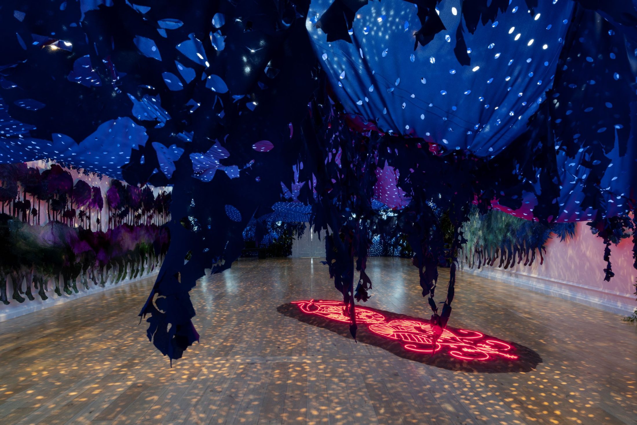 An immersive installation with blue ripped tarp hanging from the ceiling. A neon deity image glows red on the floor.